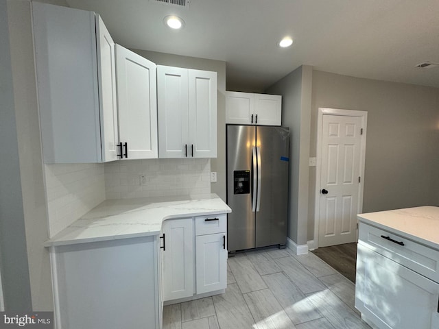 kitchen with white cabinetry, backsplash, light stone countertops, and stainless steel fridge