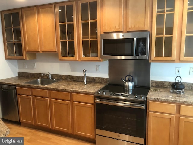 kitchen with dark stone counters, appliances with stainless steel finishes, sink, and light wood-type flooring