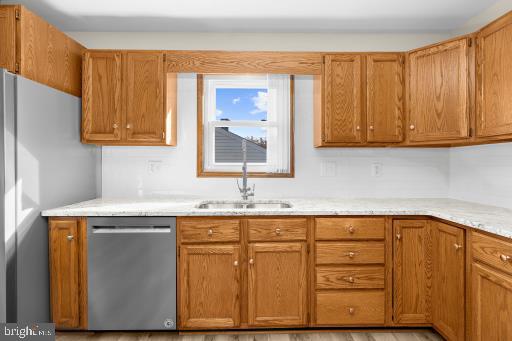 kitchen with light hardwood / wood-style flooring, stainless steel appliances, light stone countertops, and sink