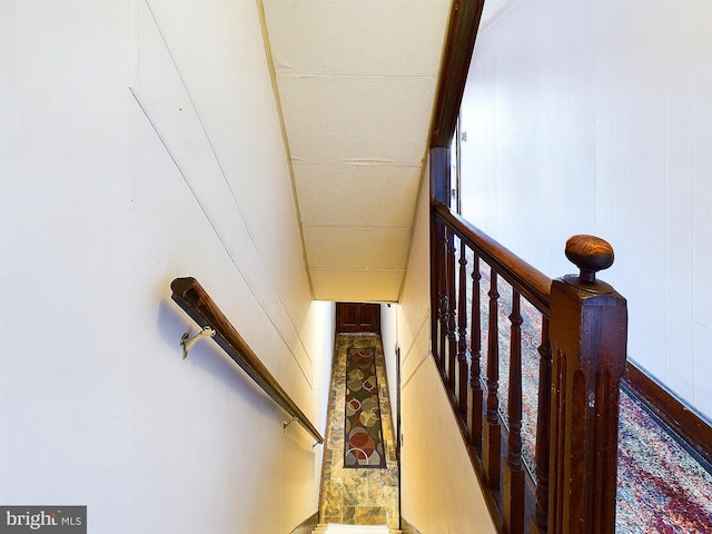 stairs with wood walls and a paneled ceiling