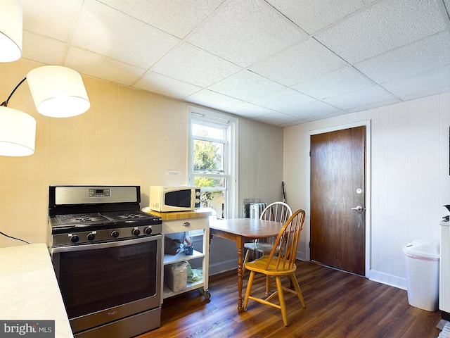 kitchen featuring stainless steel range with gas cooktop, a drop ceiling, wooden walls, and dark hardwood / wood-style flooring