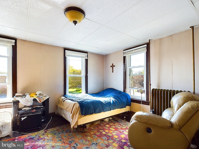 bedroom with multiple windows, radiator heating unit, and wood walls