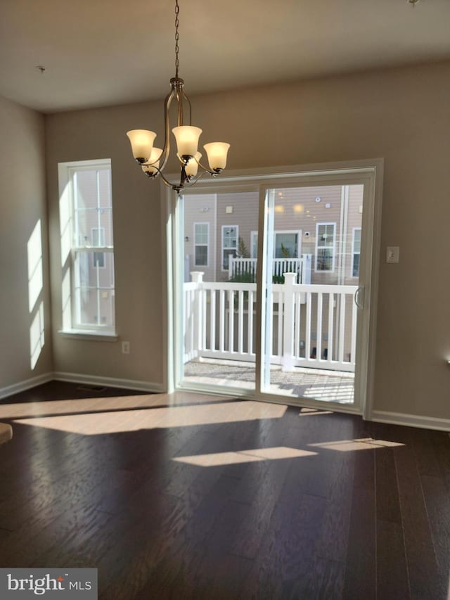 unfurnished dining area with a healthy amount of sunlight, a chandelier, and dark hardwood / wood-style flooring