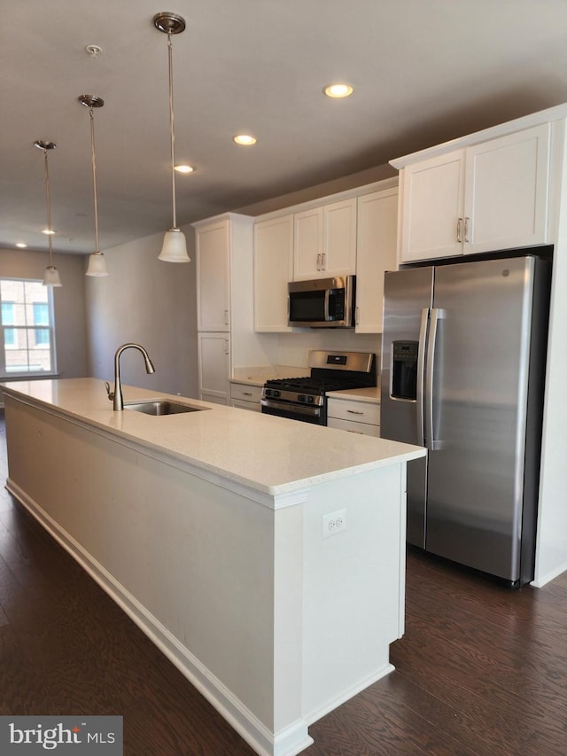 kitchen with appliances with stainless steel finishes, sink, hanging light fixtures, white cabinetry, and a kitchen island with sink