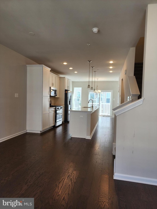 kitchen with a kitchen island with sink, hanging light fixtures, white cabinets, appliances with stainless steel finishes, and dark hardwood / wood-style flooring