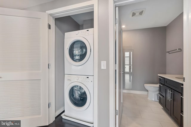 laundry room featuring stacked washing maching and dryer and light tile patterned floors