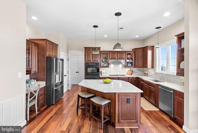 kitchen featuring visible vents, a kitchen island, a sink, stainless steel appliances, and under cabinet range hood