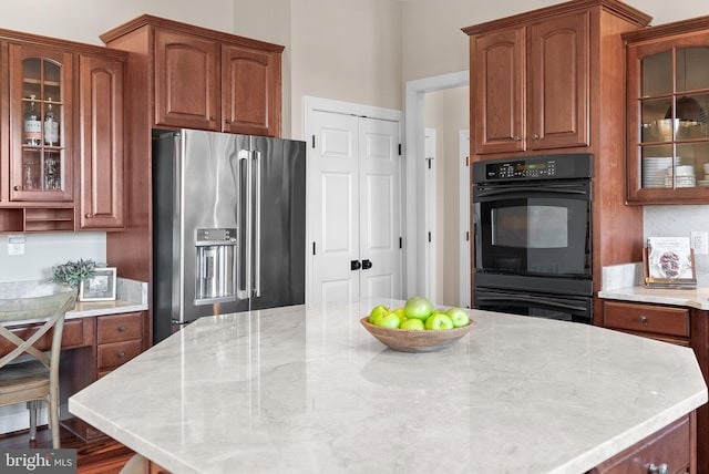 kitchen featuring light stone countertops, glass insert cabinets, dobule oven black, and stainless steel fridge with ice dispenser