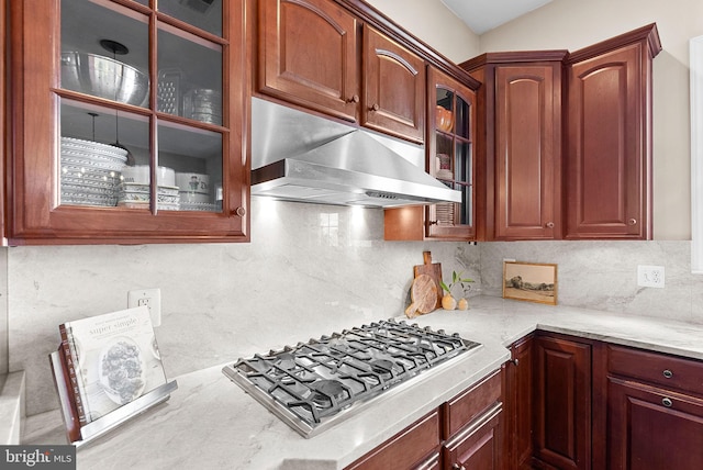 kitchen featuring stainless steel gas stovetop, exhaust hood, glass insert cabinets, and tasteful backsplash