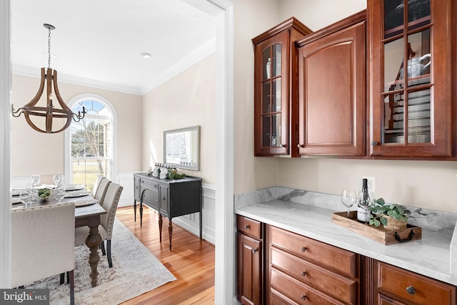 interior space with crown molding, decorative light fixtures, glass insert cabinets, and light wood-type flooring