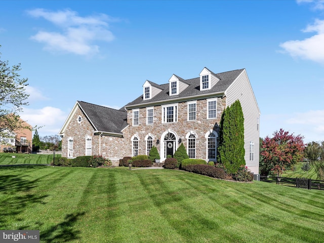 colonial-style house with stone siding, a front yard, and fence