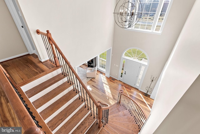 entryway featuring stairway, wood finished floors, baseboards, a towering ceiling, and a notable chandelier