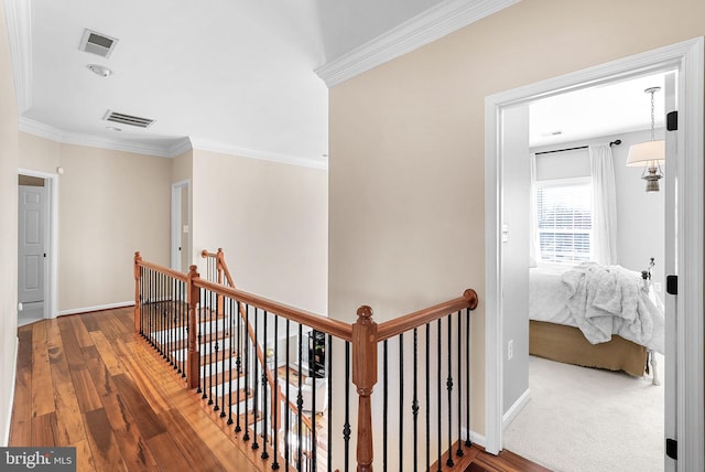 hallway featuring wood finished floors, an upstairs landing, visible vents, and ornamental molding