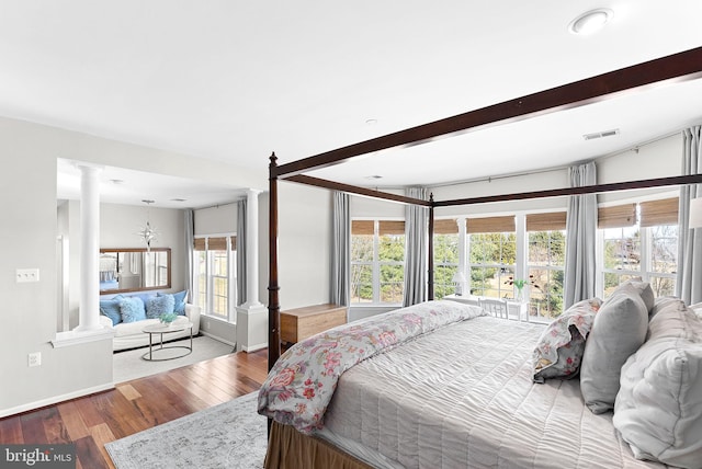 bedroom with visible vents, multiple windows, wood finished floors, and decorative columns