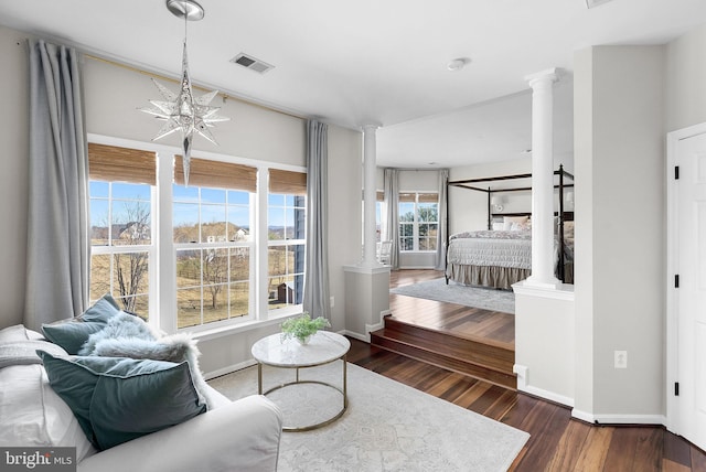 bedroom featuring decorative columns, wood finished floors, visible vents, and a chandelier