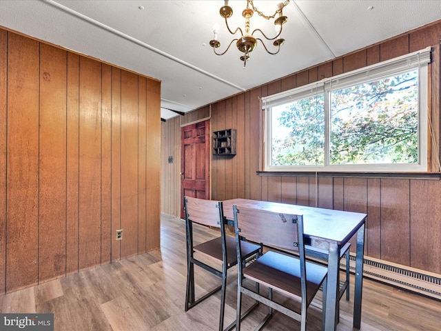 dining room featuring an inviting chandelier, wood walls, a textured ceiling, and light wood-type flooring