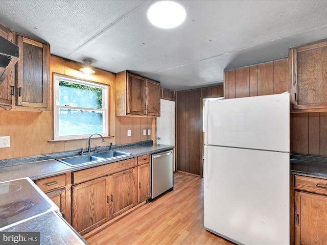 kitchen featuring dishwasher, wooden walls, sink, and white refrigerator