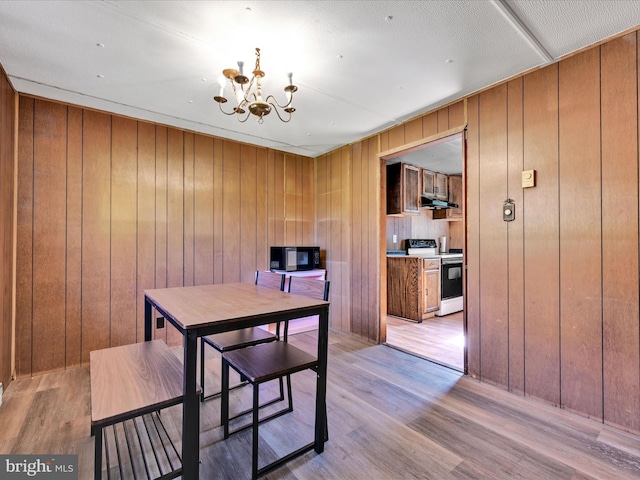 dining space with wood walls, an inviting chandelier, and light wood-type flooring