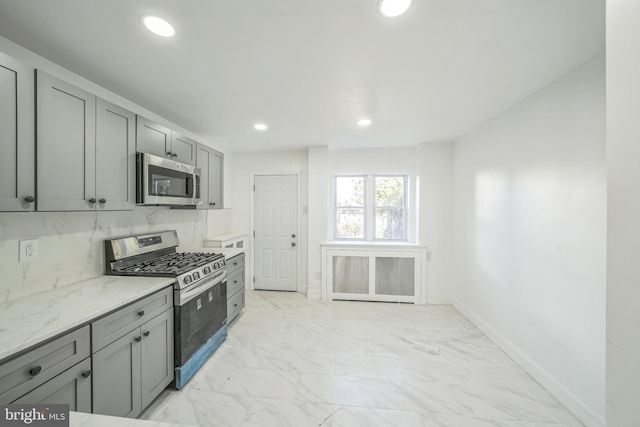 kitchen featuring gray cabinets, light stone countertops, stainless steel appliances, and backsplash