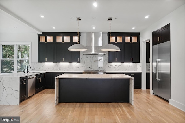 kitchen featuring pendant lighting, wall chimney range hood, light hardwood / wood-style floors, a kitchen island, and stainless steel appliances