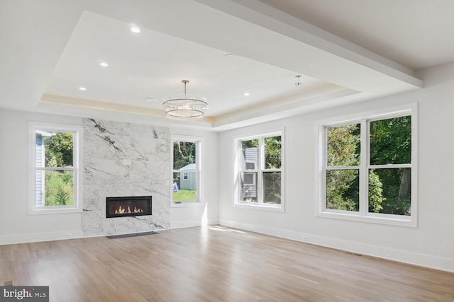 unfurnished living room with a raised ceiling, a wealth of natural light, light hardwood / wood-style flooring, and a high end fireplace