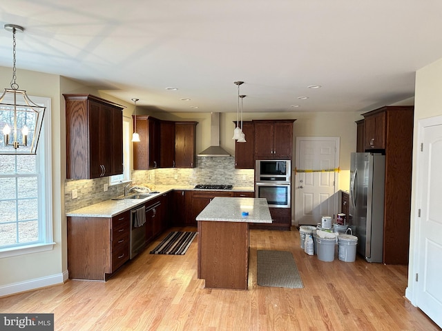 kitchen with appliances with stainless steel finishes, a kitchen island, hanging light fixtures, and wall chimney range hood