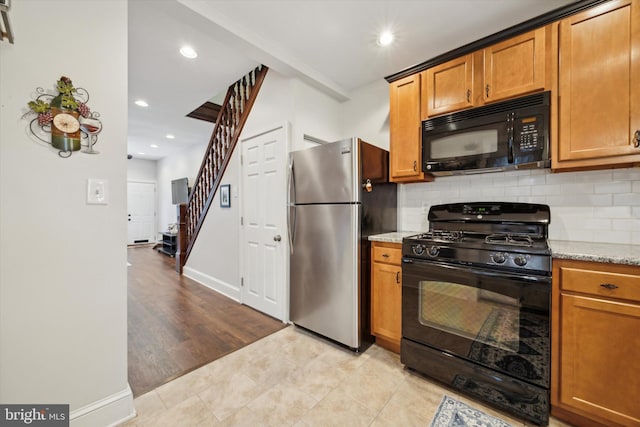 kitchen with light stone countertops, tasteful backsplash, black appliances, and light hardwood / wood-style flooring