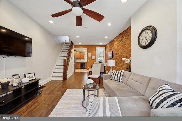 living room featuring dark wood-type flooring, ceiling fan, and brick wall