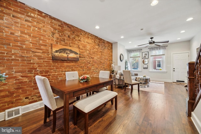 dining space with hardwood / wood-style floors, ceiling fan, and brick wall