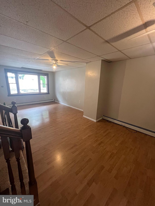 basement with baseboard heating, hardwood / wood-style floors, a paneled ceiling, and ceiling fan