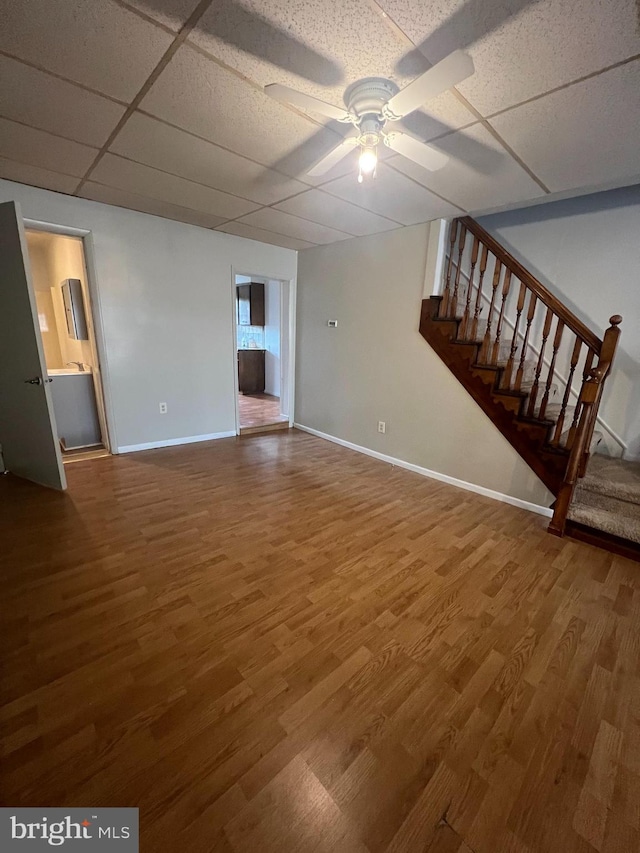 unfurnished living room with a drop ceiling, hardwood / wood-style flooring, and ceiling fan