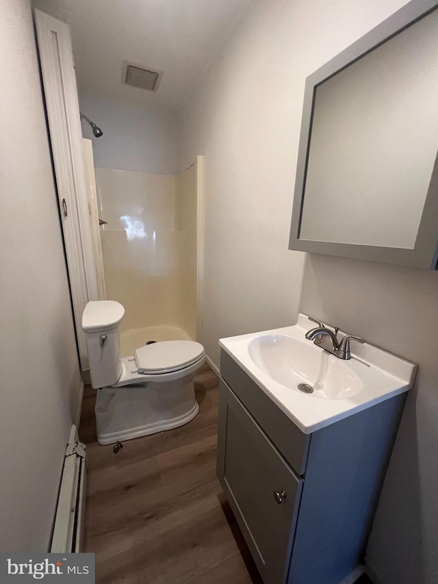 bathroom with hardwood / wood-style floors, a baseboard heating unit, a shower, toilet, and vanity