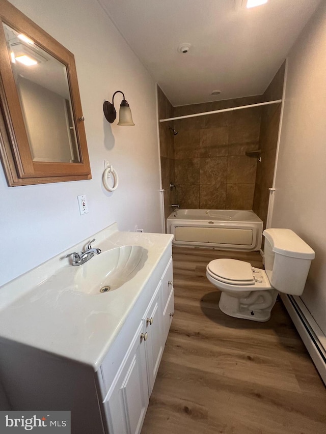 full bathroom featuring hardwood / wood-style flooring, toilet, baseboard heating, tiled shower / bath, and vanity