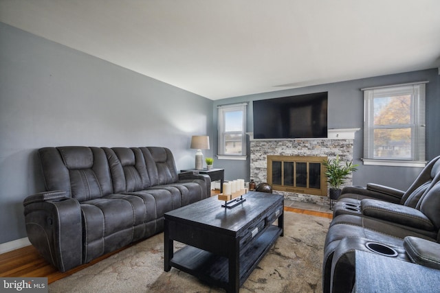 living room with a stone fireplace, wood-type flooring, and lofted ceiling