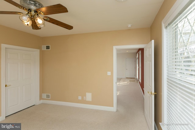 unfurnished room with a wealth of natural light, light colored carpet, and ceiling fan