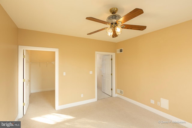 unfurnished bedroom with ceiling fan, a spacious closet, light carpet, and a closet