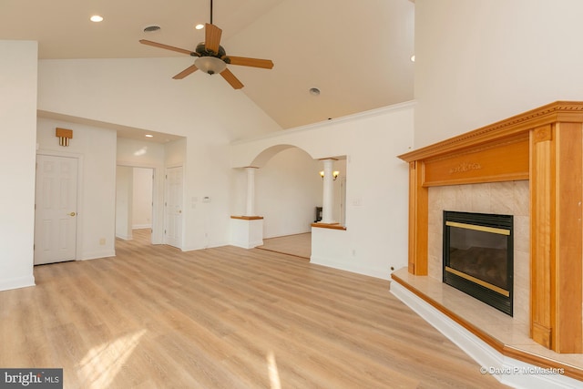 unfurnished living room with crown molding, high vaulted ceiling, light hardwood / wood-style flooring, ceiling fan, and a tiled fireplace