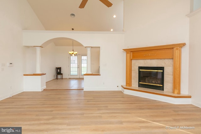 unfurnished living room with a premium fireplace, ceiling fan, light wood-type flooring, french doors, and ornate columns