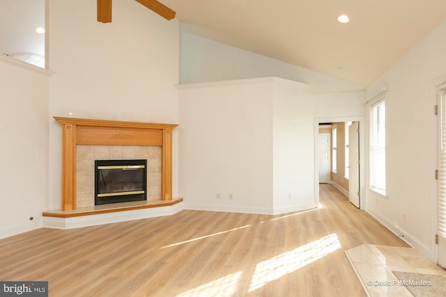 unfurnished living room featuring a tiled fireplace, high vaulted ceiling, and light wood-type flooring