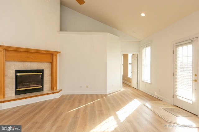 unfurnished living room featuring high vaulted ceiling, a tile fireplace, and light hardwood / wood-style flooring