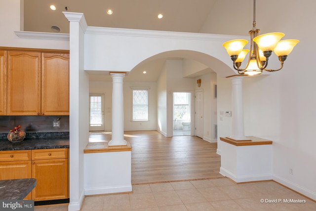 kitchen with ornamental molding, decorative light fixtures, vaulted ceiling, and ornate columns