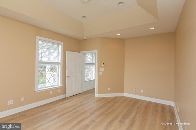 unfurnished room with a wealth of natural light, light wood-type flooring, and a tray ceiling