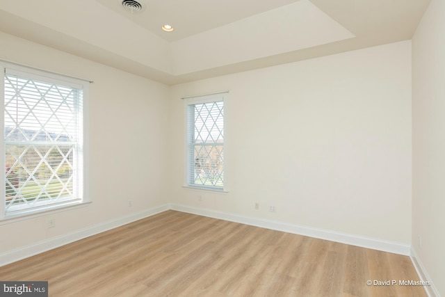 empty room with light hardwood / wood-style floors and a tray ceiling