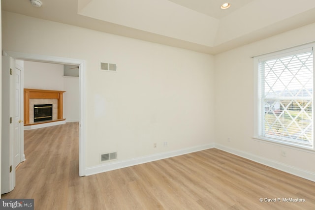 spare room with a tray ceiling, light hardwood / wood-style floors, and a tile fireplace