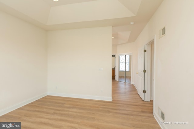 spare room with light hardwood / wood-style floors and a raised ceiling