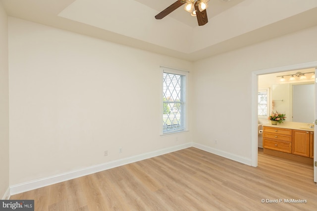 unfurnished bedroom with sink, light hardwood / wood-style flooring, ceiling fan, connected bathroom, and a raised ceiling