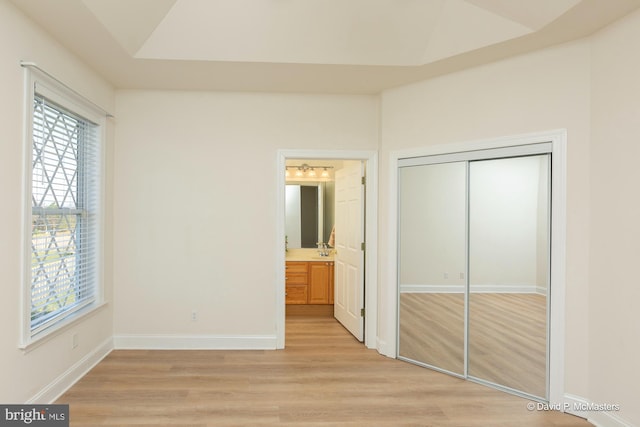 unfurnished bedroom with ensuite bathroom, light wood-type flooring, and a closet