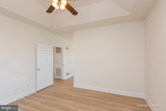 empty room featuring light hardwood / wood-style flooring, ceiling fan, and a tray ceiling