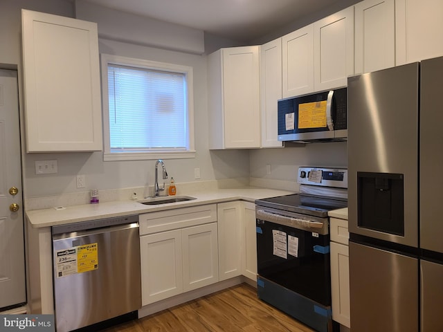 kitchen with light countertops, light wood-style flooring, appliances with stainless steel finishes, white cabinets, and a sink