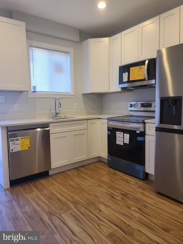 kitchen with stainless steel appliances, wood finished floors, a sink, white cabinets, and light countertops